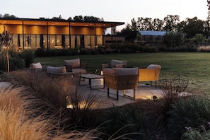 An outdoor seating area with wicker furniture and a view of a modern building. - Legado Wine Lodge (Maipú)