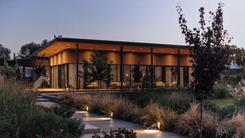 A modern building with a glass facade, a covered outdoor seating area, and a pathway leading to the entrance.