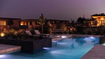 A swimming pool with lounge chairs and a stone deck, surrounded by landscaped gardens and modern buildings.