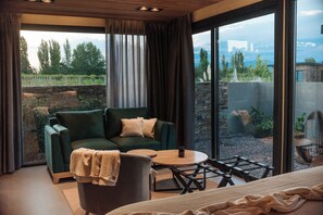 A modern room with a green sofa, a round wooden table, and a view of a garden and cityscape through large windows.