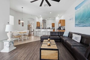 A modern living room with a black leather sofa, a wooden coffee table, and a dining area with white chairs. - Disney Princess Suite, Family Home, Sleeps 12 (Davenport)