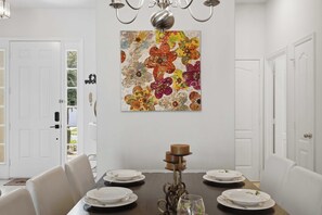 A dining room with a table set for four, a chandelier, and a colorful floral artwork on the wall. - Disney Princess Suite, Family Home, Sleeps 12 (Davenport)