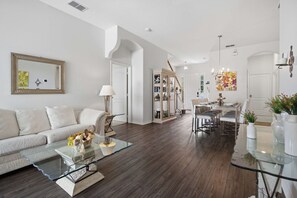 A modern living room with a glass coffee table, a white sofa, and a dining area with a chandelier. - Disney Princess Suite, Family Home, Sleeps 12 (Davenport)