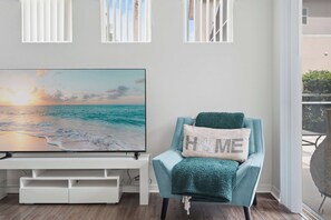 A room with a television displaying a beach scene, a teal armchair with a cushion, and a window with blinds. - Disney Princess Suite, Family Home, Sleeps 12 (Davenport)
