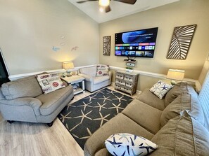 A living room with a sofa, armchair, coffee table, and a TV mounted on the wall. - Pet-Friendly Ocean Lakes 3BR | Golf Cart | Sleeps 5 (Myrtle Beach)