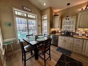 A dining area with a table and chairs, a kitchen with cabinets and appliances, and a view through the windows. - Pet-Friendly Ocean Lakes 3BR | Golf Cart | Sleeps 5 (Myrtle Beach)