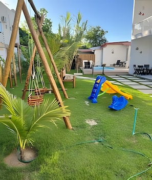 Un espace de jeux pour enfants avec des balançoires, un toboggan et une pelouse artificielle.