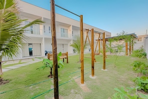 Une cour avec une balançoire en bois, un banc et, au fond, un bâtiment doté de grandes fenêtres.
