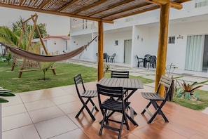 Une terrasse extérieure couverte, équipée d’une table et de chaises, d’un hamac, et offrant une vue sur l’intérieur du bâtiment.