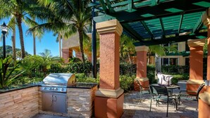 Un patio al aire libre con una parrilla, asientos y palmeras.