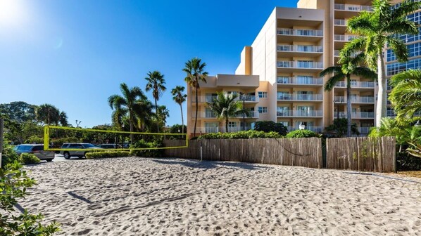 A sandy beach with a wooden fence and palm trees.