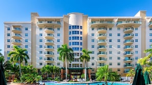 A multi-story hotel with a central courtyard, outdoor pool, and palm trees.