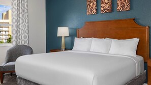 A hotel room with a large bed, a nightstand with a lamp, a chair, and a view of the outside.