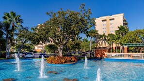 A hotel with a swimming pool, palm trees, and a fountain.