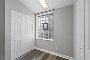 Un couloir avec une porte blanche, une fenêtre ornée d’un cadre et un luminaire au plafond.