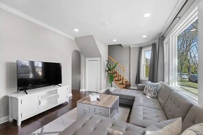 A modern living room with a flat-screen TV, a sectional sofa, a coffee table, and a staircase leading to an upper level. - Stunning open-concept  3-bedroom 2-bathroom fully equipped home in Morton Grove (Morton Grove)