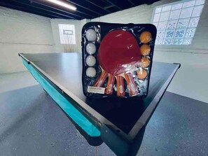 Mesa de bilhar com bolas e tacos em um salão com parede de azulejos e janela.