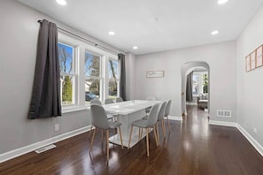 A dining area with a white table and grey chairs, large windows with curtains, and a view of the outdoors. - Stunning open-concept  3-bedroom 2-bathroom fully equipped home in Morton Grove (Morton Grove)
