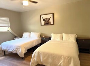 Ein Schlafzimmer mit zwei Betten, einem Deckenventilator und einem gerahmten Bild an der Wand.