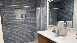 A bathroom with a shower, a sink, and a mirror. - River House (Logan)