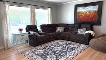 A living room with a sectional sofa, a patterned rug, a side table, and a large window with curtains.