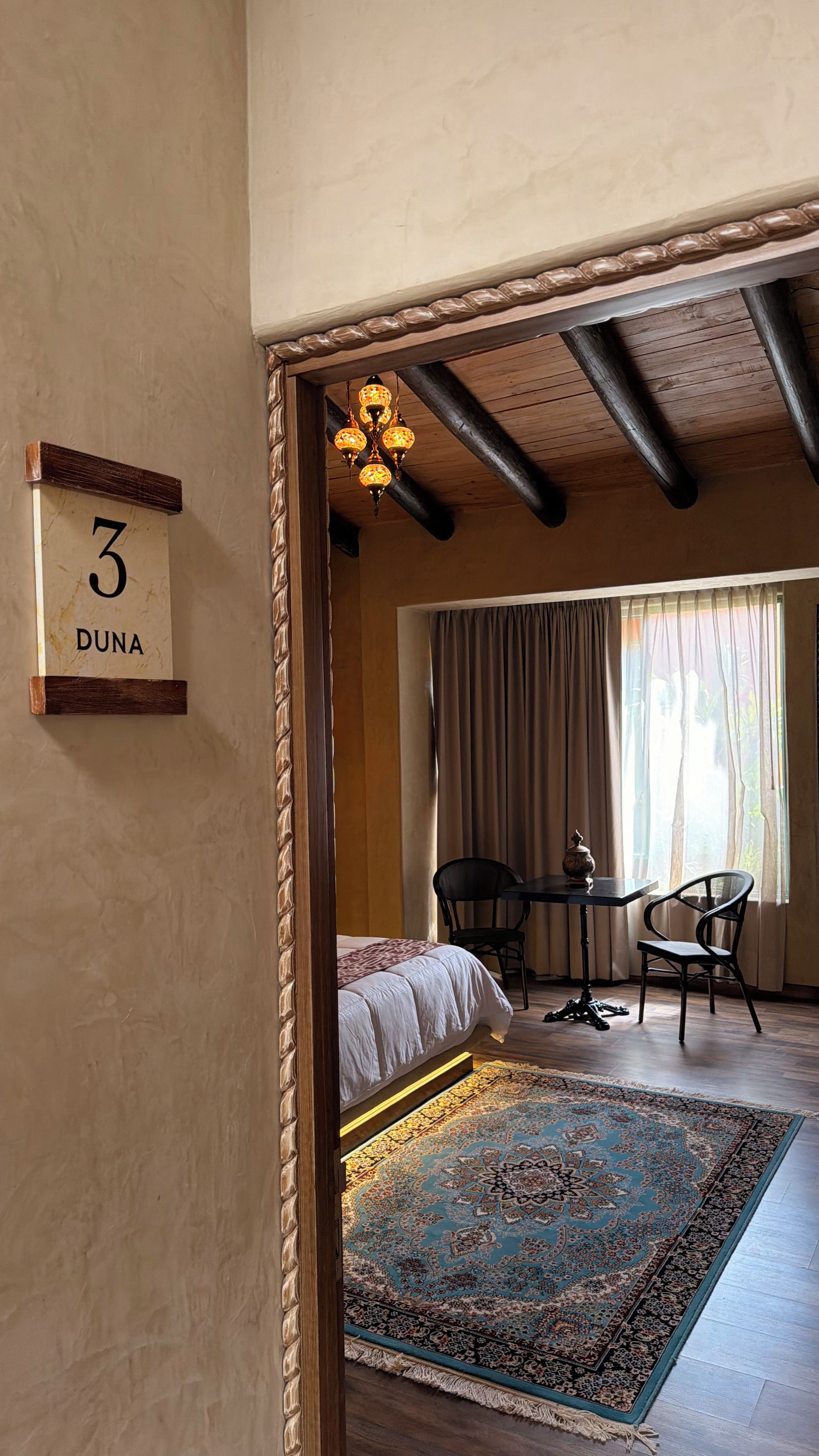 A bedroom with a bed, a table, chairs, a rug, and a chandelier.