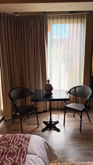 Quarto com cama, duas cadeiras, mesa e janela com cortinas.
