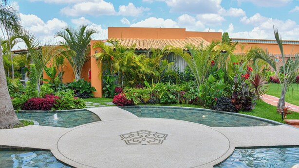 A pool area with a geometric design, surrounded by lush tropical plants and a building with a tiled roof. - La Mezquita Hotel & Spa (Jesus Maria)
