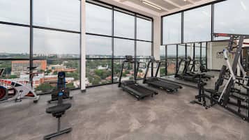 Un gimnasio con cintas de correr, máquinas de pesas y vistas de la ciudad.
