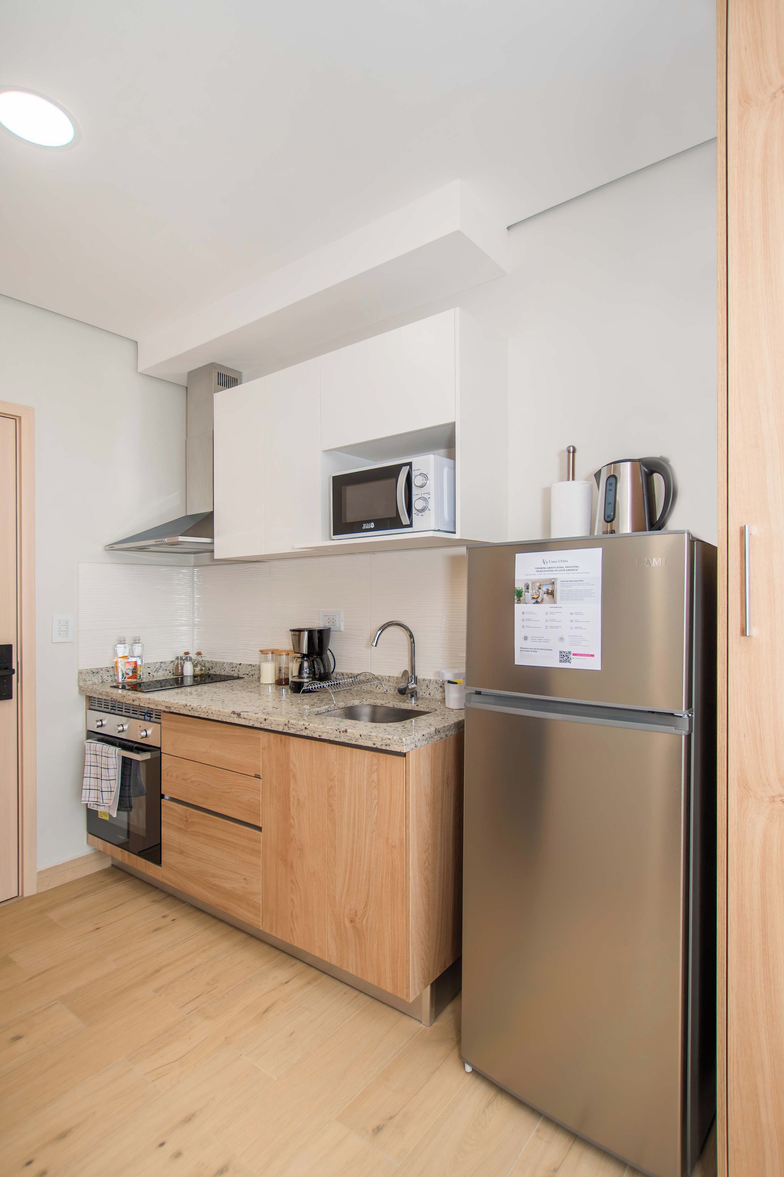 Una cocina moderna con un refrigerador de acero inoxidable, un microondas y una cafetera sobre la encimera.