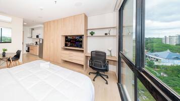Un dormitorio moderno con una cama grande, un escritorio con silla, kitchenette y un televisor con el logo de Netflix.