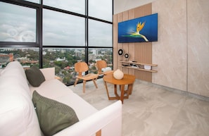Una sala de estar moderna con un ventanal grande, un sofá, dos sillones, una mesa redonda y un televisor montado.