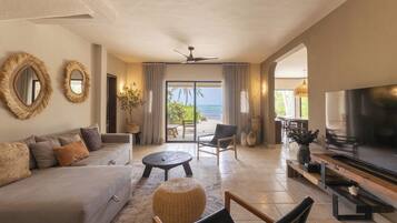 A modern living room with a sofa, chairs, a TV, and a balcony with a view of the sea.