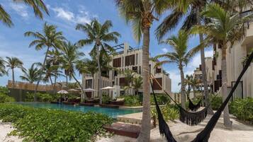 Un espace aménagé au bord de la piscine, avec un hamac, des palmiers et un bâtiment doté de balcons.