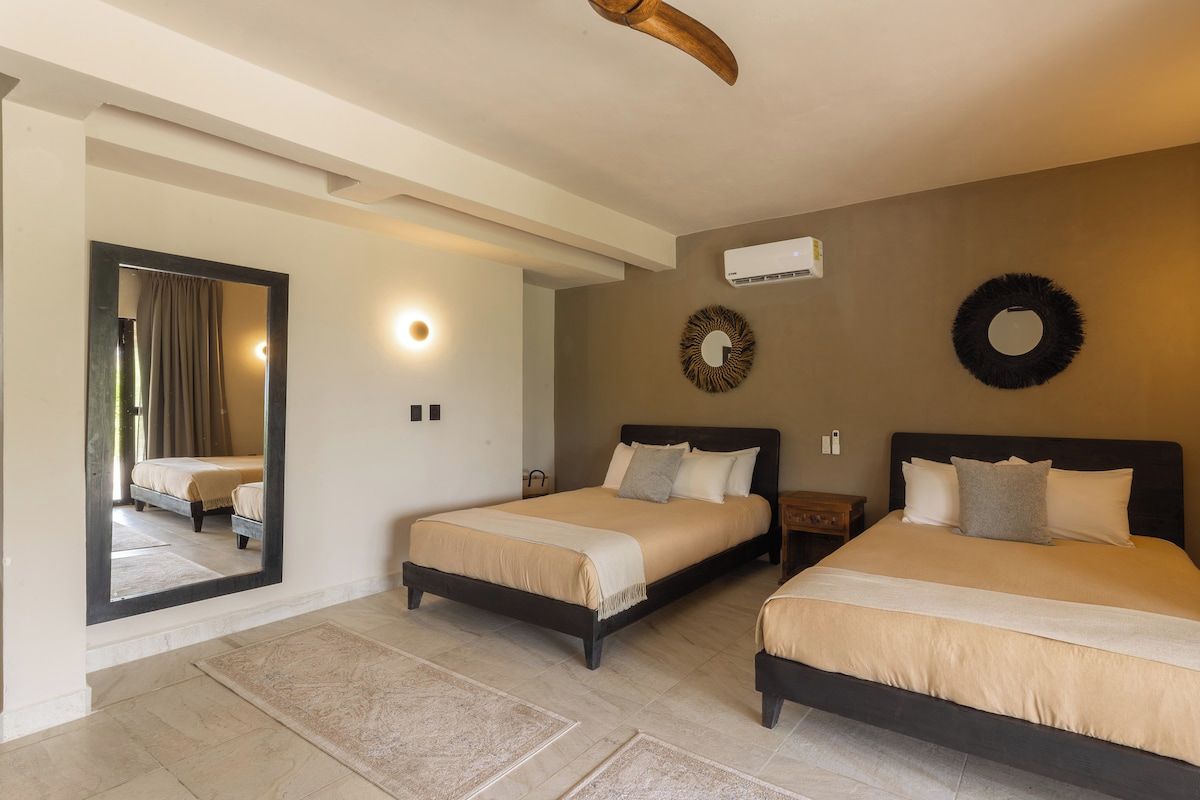 Une chambre d’hôtel avec deux lits, un miroir, un climatiseur fixé au mur et un élément décoratif circulaire sur le mur.