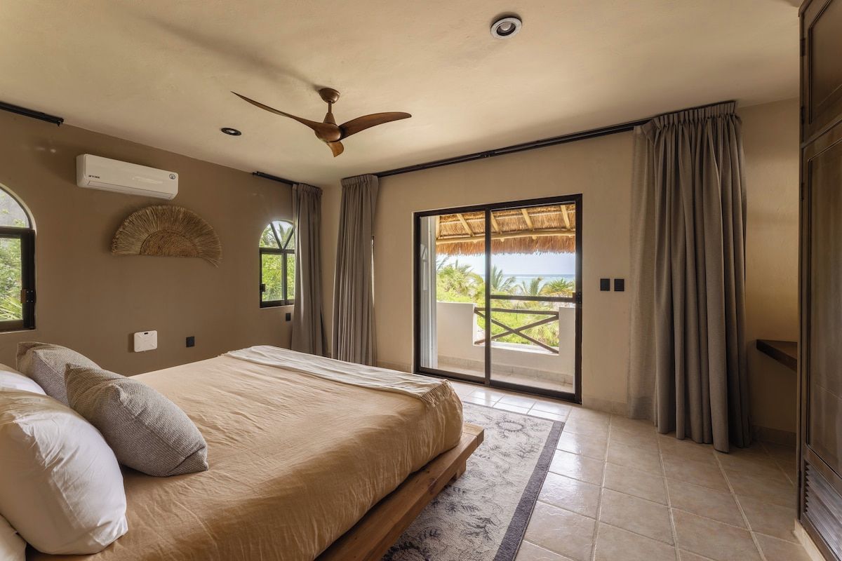 A bedroom with a bed, ceiling fan, air conditioning unit, and a sliding glass door leading to an outdoor area.