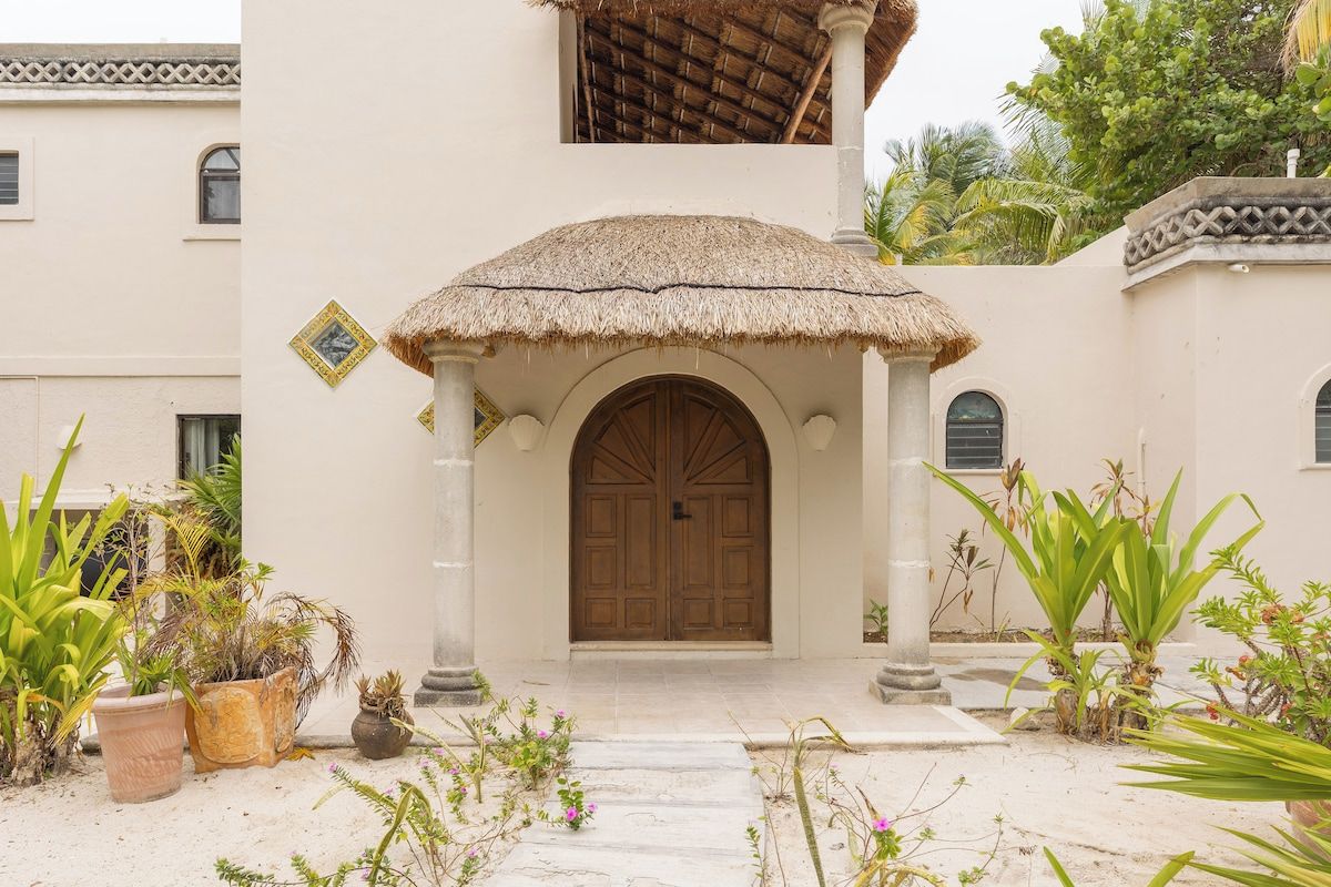 A building with a thatched roof entrance, a large wooden door, and potted plants around the entrance.