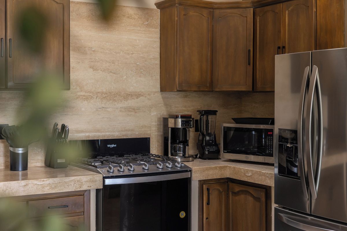 Une cuisine dotée de meubles en bois, d’un réfrigérateur en acier inoxydable, d’un four à micro-ondes, d’une machine à café et d’une cuisinière.