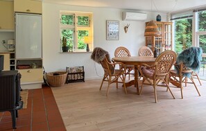 A dining area with a round wooden table surrounded by wicker chairs, a kitchen with a white refrigerator, and a window with a view of greenery. - Lovely home in Roslev with house a panoramic view (Roslev)