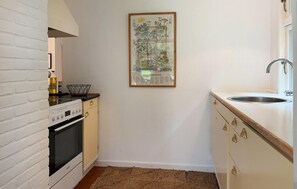 Cocina compacta con pared de ladrillo blanco, estufa, lavamanos e ilustración botánica enmarcada en la pared.