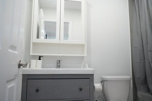 Ein Badezimmer mit weißem Waschbecken, einem Spiegel, einer Toilette und einer Duschvorhang.