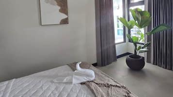 Una camera d'albergo con un letto, una pianta in vaso, un quadro appeso e una finestra con tende.