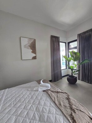 A hotel room with a bed, a potted plant, a painting on the wall, and a window with curtains.