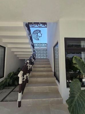 A modern staircase with a geometric railing design, leading to a balcony with a decorative head silhouette.