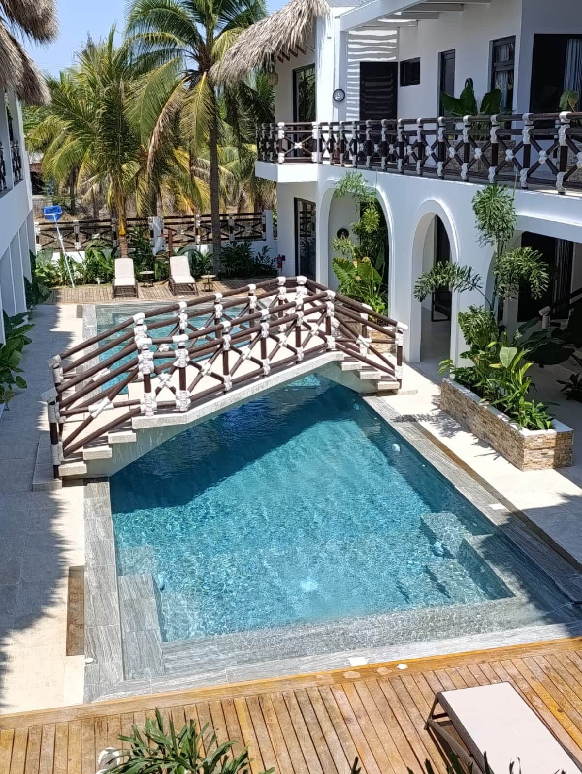 Ein Swimmingpool mit Holzterrasse, umgeben von Liegestühlen und Palmen.