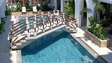 Ein Swimmingpool mit Holzterrasse, umgeben von Liegestühlen und Palmen.