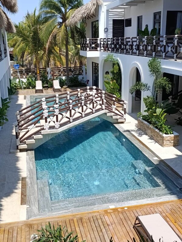 A swimming pool with a wooden deck, surrounded by lounge chairs and palm trees.