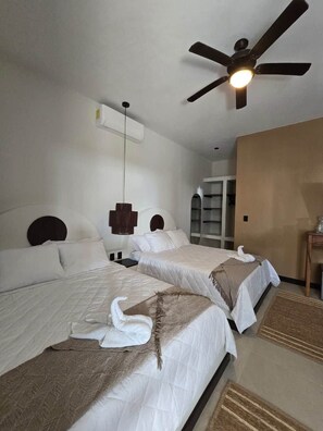 Habitación de hotel con dos camas, ventilador de techo, aire acondicionado de pared y un mueble de almacenamiento.