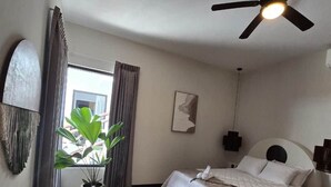 Ein Hotelzimmer mit Bett, Deckenventilator, Blumentopf und Blick ins Freie.