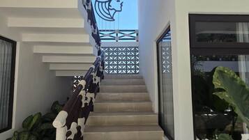 Un escalier moderne doté d’une rampe au design géométrique, menant à un balcon orné d’une silhouette décorative en forme de tête.